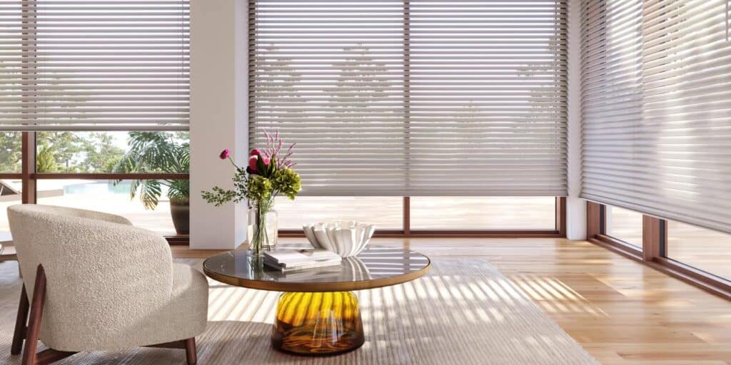 Bright airy space with natural sunlight filtering through horizontal blinds, minimalistic decor, wooden flooring, and lush greenery outside.