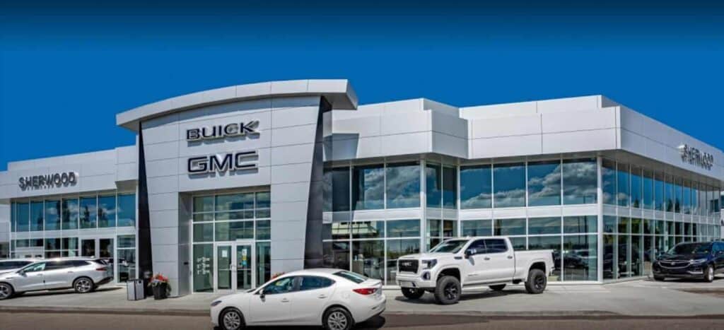Modern Sherwood Buick GMC dealership with large glass windows and multiple vehicles parked outside, showcasing a wide selection of new and used cars.